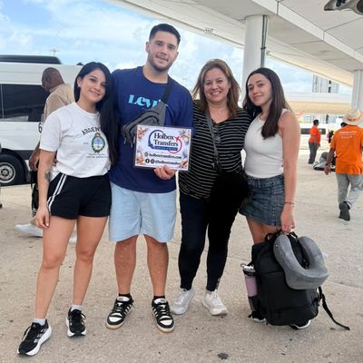 Una familia alegre posa con el banner de Holbox Transfers en la terminal del aeropuerto, con el equipaje listo para el viaje a Holbox.