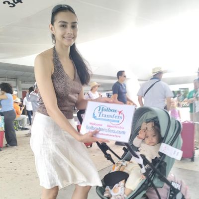 Familia llegando a la terminal, la mamá sostiene el banner de Holbox Transfers junto a la carriola de su bebé antes del trayecto a Holbox.