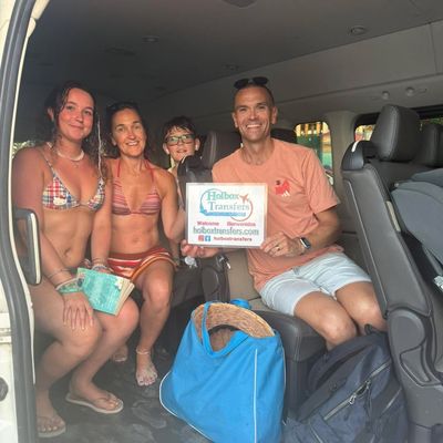 Familia en ropa de playa sonríe dentro de la van sosteniendo el banner de Holbox Transfers, relajados tras un día de sol cerca de Holbox.