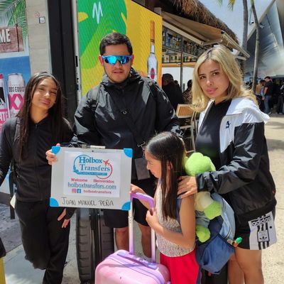 Familia de cuatro sosteniendo el banner de Holbox Transfers en la terminal, equipaje en mano, lista para partir a Holbox.