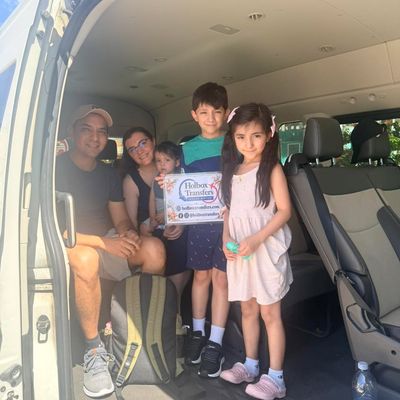 Familia reunida dentro de la van, los niños sostienen con orgullo el banner de Holbox Transfers antes del traslado a Holbox.