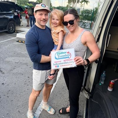 Familia reunida junto a la puerta abierta de la van, sosteniendo el banner de Holbox Transfers mientras comienza su viaje a Holbox.