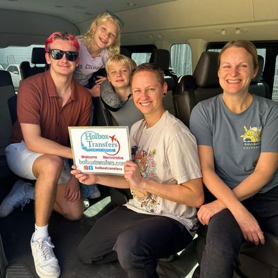 Una familia reunida dentro de la van sostiene con orgullo el banner de Holbox Transfers en la ruta a Holbox.