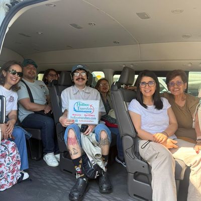 Grupo familiar sonriendo junto y sosteniendo el banner de Holbox Transfers dentro de la van durante su traslado a Holbox.
