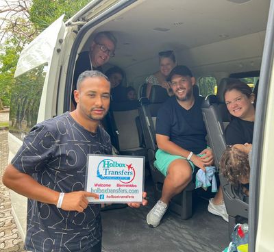 Familia sosteniendo junta el banner de Holbox Transfers dentro de la van, lista para su traslado a Holbox.