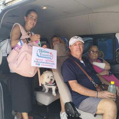 Una familia sostiene el banner de Holbox Transfers dentro de la van, con su perrito acompañándolos en el trayecto a Holbox.