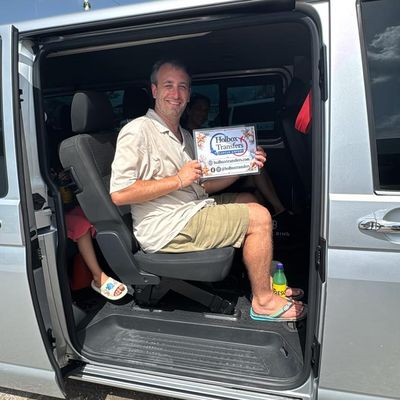 Una familia sostiene el banner de Holbox Transfers dentro de la van, un pequeño asomándose desde el asiento rumbo a Holbox.