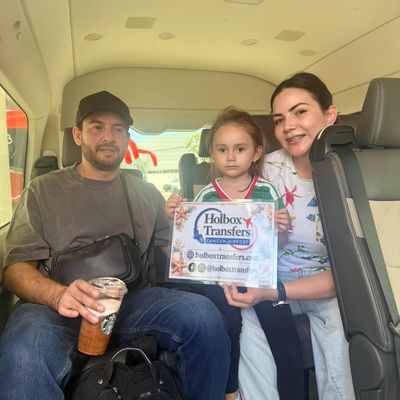 Una familia sostiene el banner de Holbox Transfers dentro de la van, la pequeña sonriendo mientras van rumbo a Holbox.