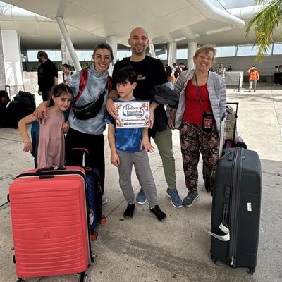 Una familia sostiene el banner de Holbox Transfers en la terminal, con maletas en mano mientras se preparan para salir hacia Holbox.
