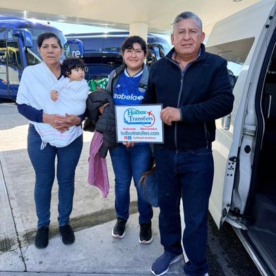Una familia sostiene junta el banner de Holbox Transfers en la terminal del aeropuerto, recibida para su viaje a Holbox.