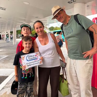 Una familia sostiene el banner de Holbox Transfers bajo el techo de la terminal, dos niños sonriendo al comenzar su viaje a Holbox.