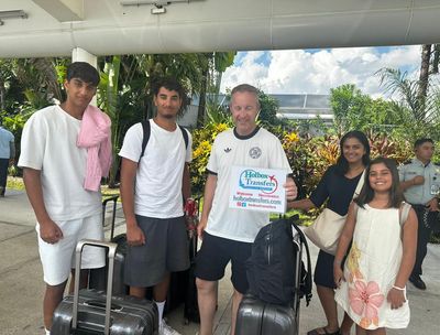 Familia con equipaje se reúne alrededor del banner de Holbox Transfers en la terminal del aeropuerto, sonriendo al comenzar su viaje a Holbox.