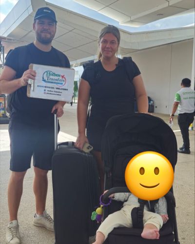 Familia posa con su carriola junto al banner de Holbox Transfers en la terminal del aeropuerto antes de partir a Holbox.