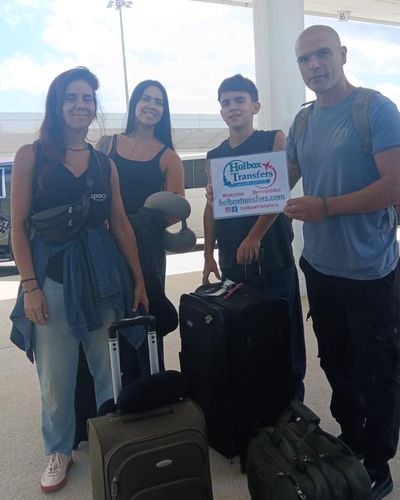 Familia posa junta en la terminal del aeropuerto con su equipaje, sosteniendo el banner de Holbox Transfers antes de partir a Holbox.