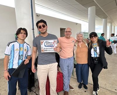 Familia posando en la terminal con el banner de Holbox Transfers, lista para comenzar su travesía a Holbox.