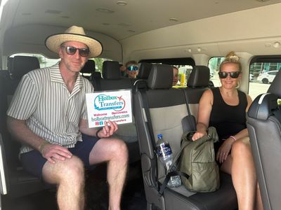 Una familia se relaja en la van sosteniendo el banner de Holbox Transfers, los niños sonriendo detrás en ruta a Holbox.