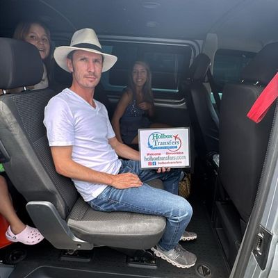 Familia relajada dentro de la van, el papá sostiene el banner de Holbox Transfers mientras parten rumbo a Holbox.