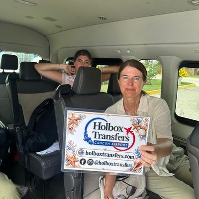 Familia relajada dentro de la van, sosteniendo el banner de Holbox Transfers mientras recorren la ruta del Aeropuerto de Cancún a Holbox.