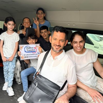 Una familia con varios niños sostiene el banner de Holbox Transfers dentro de la van, sonriendo antes del viaje a Holbox.
