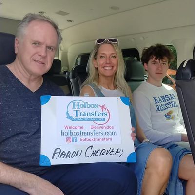 Una familia sentada dentro de la van sostiene el banner de Holbox Transfers, lista para el trayecto a Holbox.