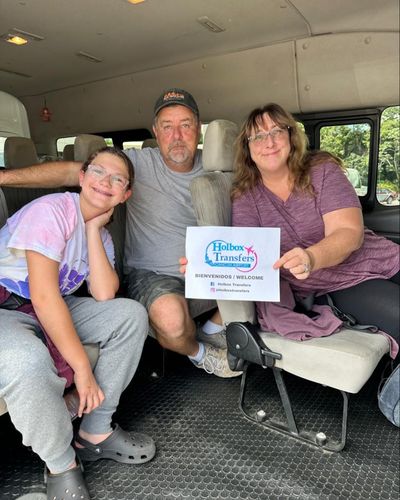 Familia sentada junta dentro de la van, sosteniendo en alto el banner de Holbox Transfers en su trayecto rumbo a Holbox.