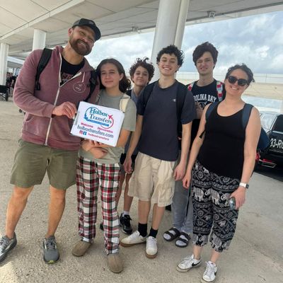 Familia sonríe junta en la terminal del aeropuerto, sosteniendo el banner de Holbox Transfers mientras se preparan para viajar a Holbox.