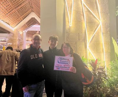 Familia sonríe junta sosteniendo el banner de Holbox Transfers entre luces festivas en su destino en Akumal.