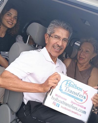 Familia sonríe junta dentro de la van, sosteniendo el banner de Holbox Transfers mientras viajan rumbo a Isla Mujeres (Puerto Juárez).