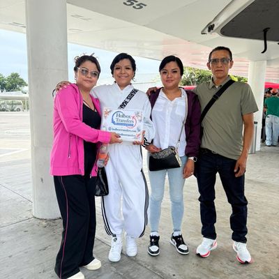 Familia de pie junta en la terminal, sosteniendo el banner de Holbox Transfers antes de emprender el camino a Holbox.