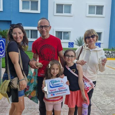Familia con dos niños sostiene el banner de Holbox Transfers afuera de su alojamiento tras llegar con bien a Holbox.