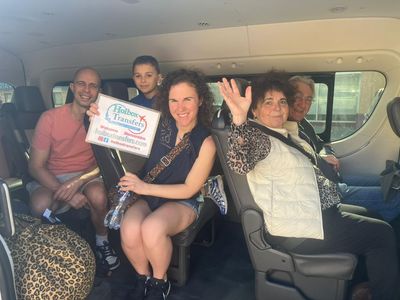 Familia saluda y sonríe dentro de la van, sosteniendo el banner de Holbox Transfers durante su traslado Zona Hotelera de Cancún - Ferry de Puerto Juárez.