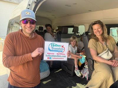 El papá sostiene el banner de Holbox Transfers junto a la van mientras la familia se acomoda para el viaje a Holbox.