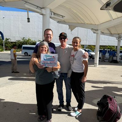 Grupo de amigos se abraza sosteniendo el banner de Holbox Transfers en la terminal del aeropuerto, sonriendo antes del viaje a Holbox.