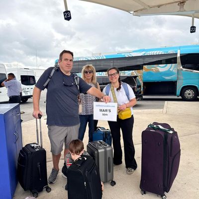 Grupo de amigos reunido bajo el techo de la terminal con mochilas, sosteniendo el banner de Holbox Transfers antes de salir hacia Holbox.