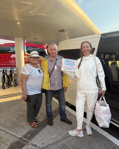 Grupo de amigos reunido alrededor del banner de Holbox Transfers afuera de la terminal del aeropuerto, listos para partir rumbo a Holbox.