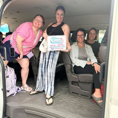 Grupo de amigos reunido dentro de la van, uno sostiene el banner de Holbox Transfers mientras sonríen en ruta a Holbox.