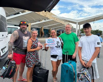 Grupo de amigos reunido con equipaje en la terminal, sosteniendo el banner de Holbox Transfers para el traslado Aeropuerto de Cancún - Holbox.