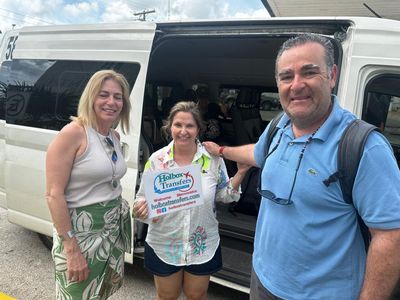 Un grupo de amigos sostiene el banner de Holbox Transfers junto a la puerta abierta de la van, a punto de salir hacia Playa del Carmen.