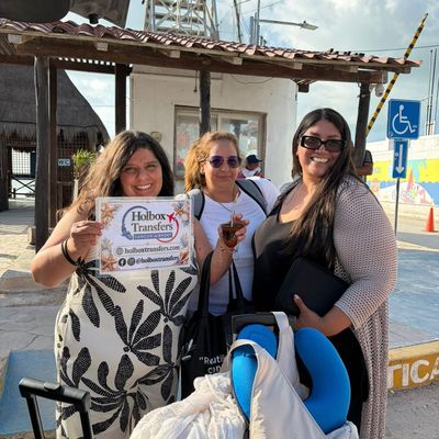 Un grupo de amigos sostiene el banner de Holbox Transfers en el muelle del ferry, sonriendo antes de cruzar a Holbox.