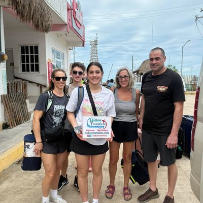 Grupo de amigos sostiene el banner de Holbox Transfers cerca del muelle del ferry, equipaje en mano, listos para cruzar a Holbox.