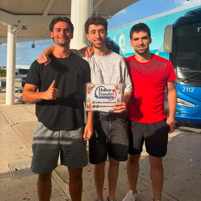 Un grupo de amigos sostiene el banner de Holbox Transfers afuera de la terminal, puras sonrisas antes de su viaje a Holbox.