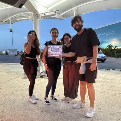Un grupo de amigos sostiene el banner de Holbox Transfers afuera de la terminal al atardecer, sonriendo antes de partir a Holbox.