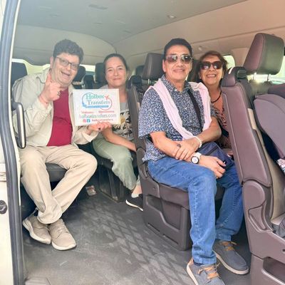 Grupo de amigos posa junto dentro de la van, sosteniendo en alto el banner de Holbox Transfers en el traslado Aeropuerto de Cancún - Holbox.