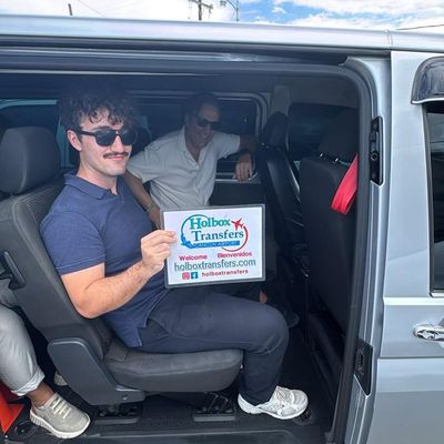 Grupo de amigos sentado dentro de la van, sonriendo mientras sostienen el banner de Holbox Transfers antes de su trayecto a Holbox.