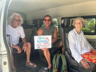 Un grupo de amigos sentado junto en la van sostiene el banner de Holbox Transfers, sonriendo camino a Holbox.