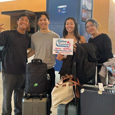 Grupo de amigos sonríe junto en la terminal, sosteniendo el banner de Holbox Transfers al llegar para su viaje a Holbox.