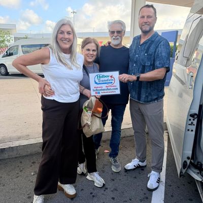 Grupo de amigos sonríe sosteniendo el banner de Holbox Transfers junto a la van en la terminal del aeropuerto, traslado Aeropuerto de Cancún - Holbox.
