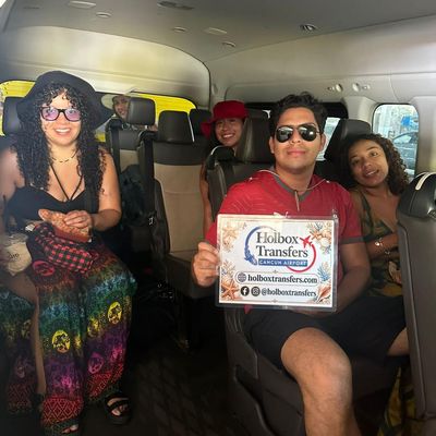 Grupo de amigos sonríe dentro de la van sosteniendo el banner de Holbox Transfers, felices en el traslado Puerto Juárez - Chiquilá (Holbox).