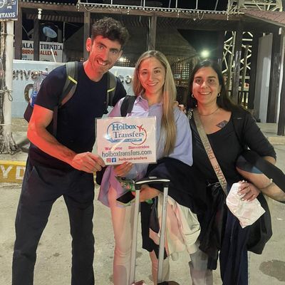 Grupo de amigos sonríe junto en el muelle del ferry por la noche, sosteniendo el banner de Holbox Transfers tras llegar cerca de Holbox.