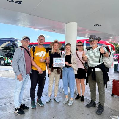 Grupo de amigos sonriendo con el banner de Holbox Transfers en la terminal del aeropuerto antes de su traslado del Aeropuerto de Cancún a Holbox.